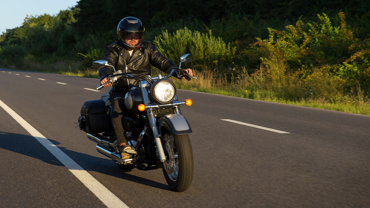 Man riding motorcycle on open road wearing black leather jacket and helmet hanging out with pals on sunny day