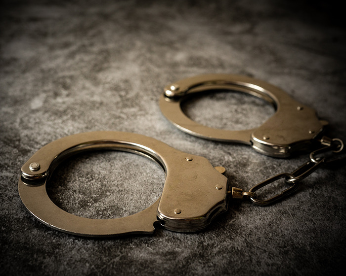 Silver handcuffs on a dark textured surface symbolizing a Batman villain turning himself in for homicide. Silver handcuffs on a dark textured surface symbolizing a Batman villain turning himself in for homicide.