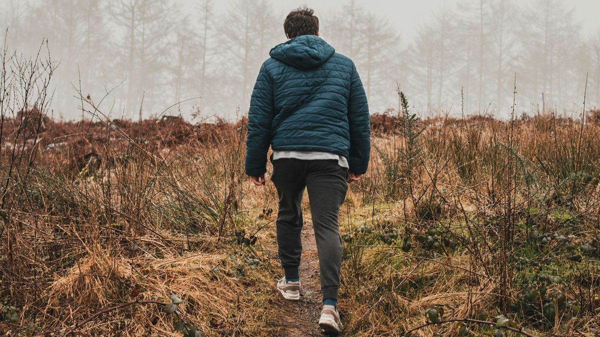 Man walking on a trail in nature wearing a blue jacket, testing effects of walking 250k steps in a week on his body