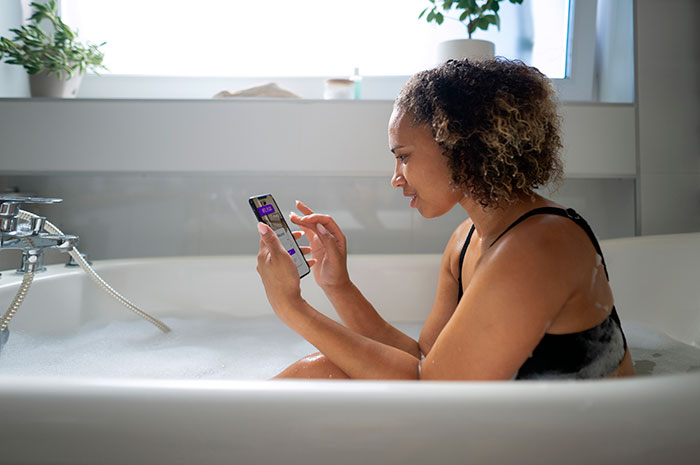 Heavily pregnant woman sitting in bathtub using smartphone, looking concerned while surrounded by bubbles. Heavily pregnant woman sitting in bathtub using smartphone, looking concerned while surrounded by bubbles.
