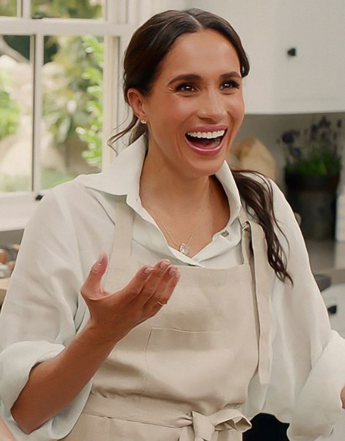 Meghan Markle smiling in a kitchen wearing an apron, related to cooking show and Pamela Anderson accusations. Meghan Markle smiling in a kitchen wearing an apron, related to cooking show and Pamela Anderson accusations.