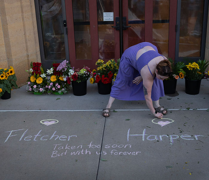 Woman in purple dress drawing hearts with chalk at memorial site for Minneapolis school attacker victims on sidewalk with flowers. Woman in purple dress drawing hearts with chalk at memorial site for Minneapolis school attacker victims on sidewalk with flowers.