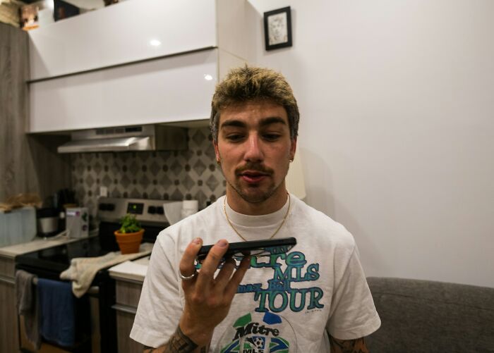 Young man in casual clothing speaking into a smartphone, highlighting performative behaviors in society discussion.