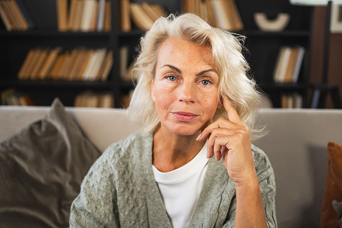 Older woman with thoughtful expression sitting on a couch, related to man never believes mom is poisoning his wife story. Older woman with thoughtful expression sitting on a couch, related to man never believes mom is poisoning his wife story.