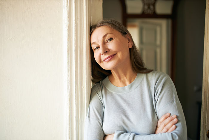 Middle-aged woman leaning against a wall with arms crossed, hinting at a story about poisoning and family conflict. Middle-aged woman leaning against a wall with arms crossed, hinting at a story about poisoning and family conflict.