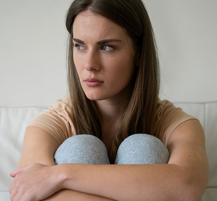 Young woman looking concerned and distant, sitting with knees hugged, reflecting tension related to poisoning and family conflict. Young woman looking concerned and distant, sitting with knees hugged, reflecting tension related to poisoning and family conflict.