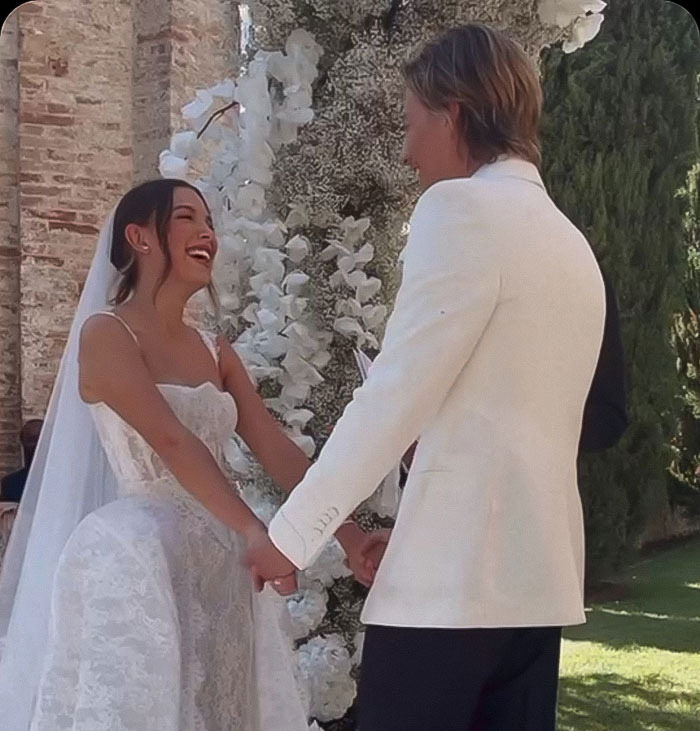 Young couple holding hands at outdoor wedding, with bride smiling in white lace dress and groom in white jacket. Young couple holding hands at outdoor wedding, with bride smiling in white lace dress and groom in white jacket.