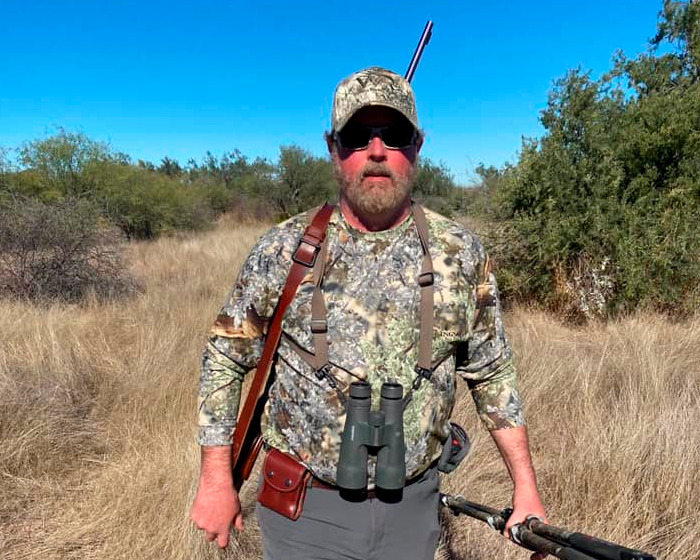 Millionaire trophy hunter in camouflage with rifle and binoculars on a safari hike in tall grass and blue sky. Millionaire trophy hunter in camouflage with rifle and binoculars on a safari hike in tall grass and blue sky.
