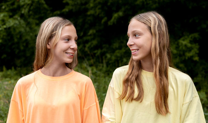 Two teenage girls smiling at each other outdoors, illustrating a story about a lady calling son disgusting for carrying pads.