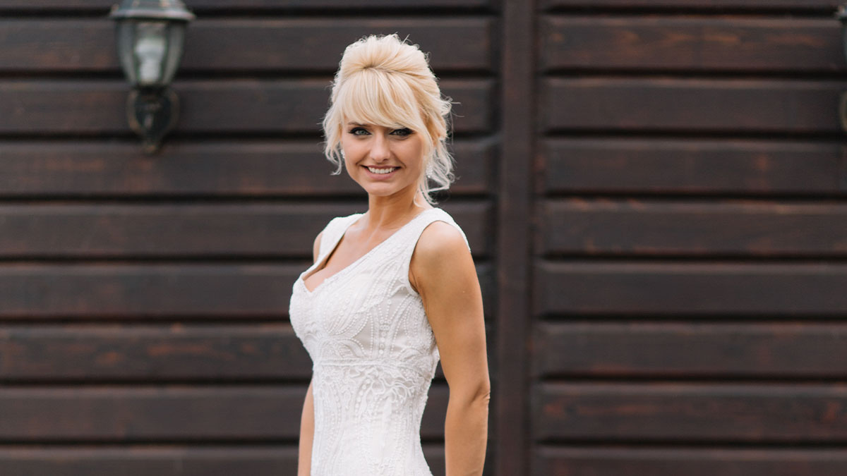 Bride smiling in detailed white gown outdoors, related to bride's mom threatening to wear white at wedding event.