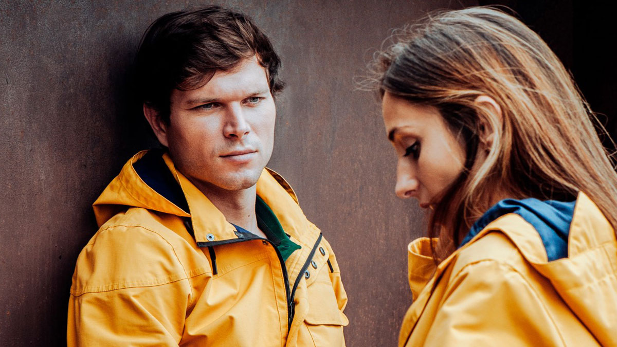 A man and woman in yellow jackets, both looking serious, illustrating themes of love and savage rejection.