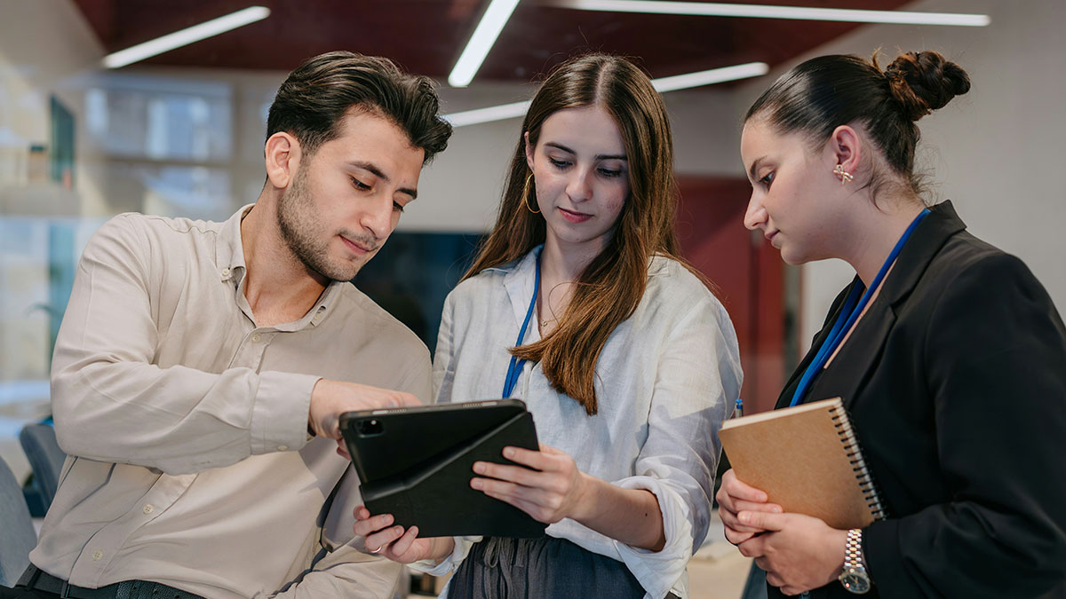 Three young professionals discussing mind tricks while looking at a digital tablet in a modern office setting.