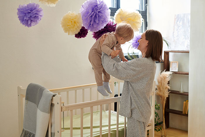 Mom holding baby near crib in decorated room, highlighting mom disables MIL’s baby cam access for privacy. Mom holding baby near crib in decorated room, highlighting mom disables MIL’s baby cam access for privacy.