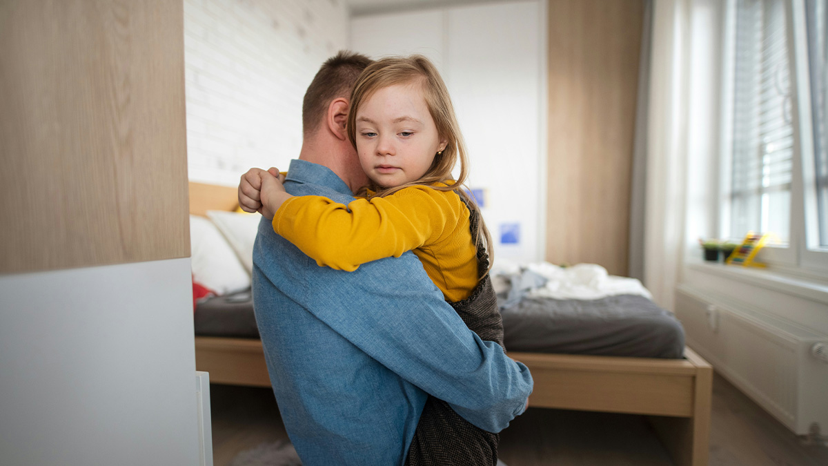 Father holding his daughter in a bedroom, showing emotional family moment reflecting mom loves girly daughter more.