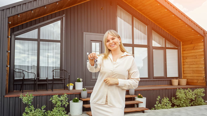 Homeowner smiling and holding keys in front of modern house, confident after dealing with entitled neighbor over fence dispute