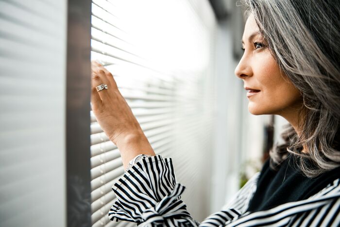 Woman frustrated looking through blinds at large neighbor's playhouse blocking privacy in residential setting. Woman frustrated looking through blinds at large neighbor's playhouse blocking privacy in residential setting.