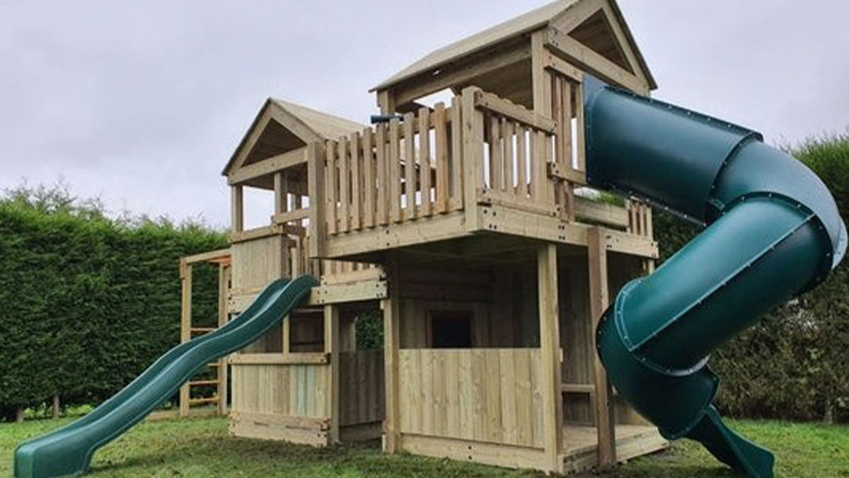 Large wooden playhouse with slides overshadowing nearby houses, affecting privacy of neighbors in suburban backyard.