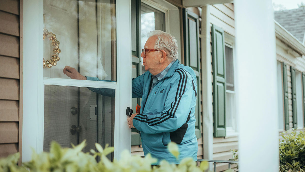 Older man in blue jacket knocking on a house door, representing a nasty neighbor in a yard dispute scenario.
