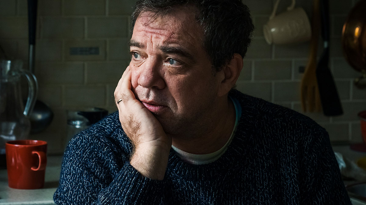 Middle-aged man looking upset in a kitchen, reflecting on relationship struggles and refusing daughter's marriage in his yard.