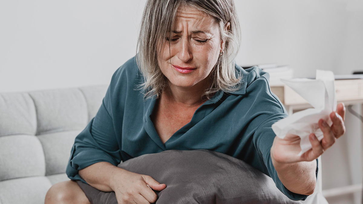 Woman upset sitting on couch holding tissue, reflecting emotional struggle in wedding venue dispute over cheating ex.