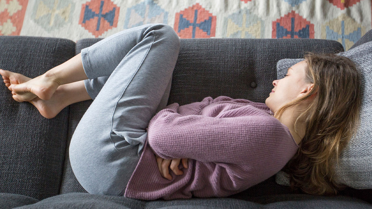 Woman in casual clothes lying curled up on a couch, representing everyday sexism and pressure women face.