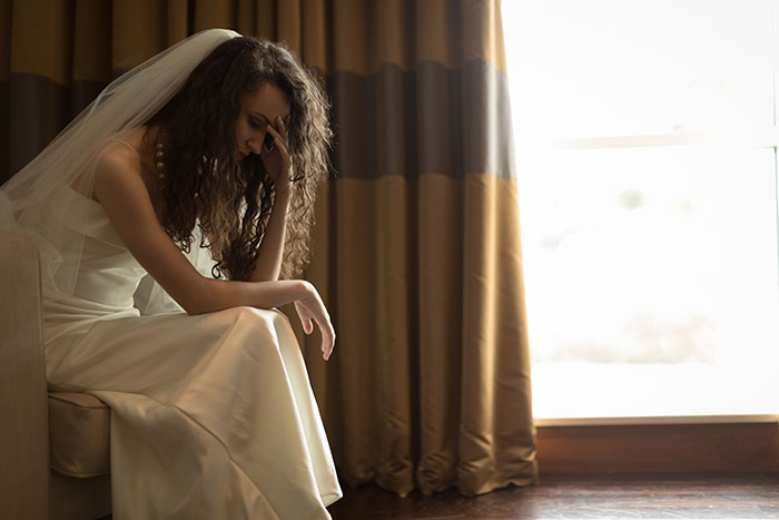 Bride in wedding dress sitting with head in hand, showing distress after woman suddenly turns flaky and misses event. Bride in wedding dress sitting with head in hand, showing distress after woman suddenly turns flaky and misses event.