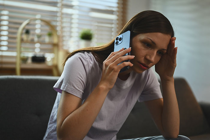 Woman looking stressed while talking on phone, appearing flaky and upset in a dimly lit living room setting. Woman looking stressed while talking on phone, appearing flaky and upset in a dimly lit living room setting.