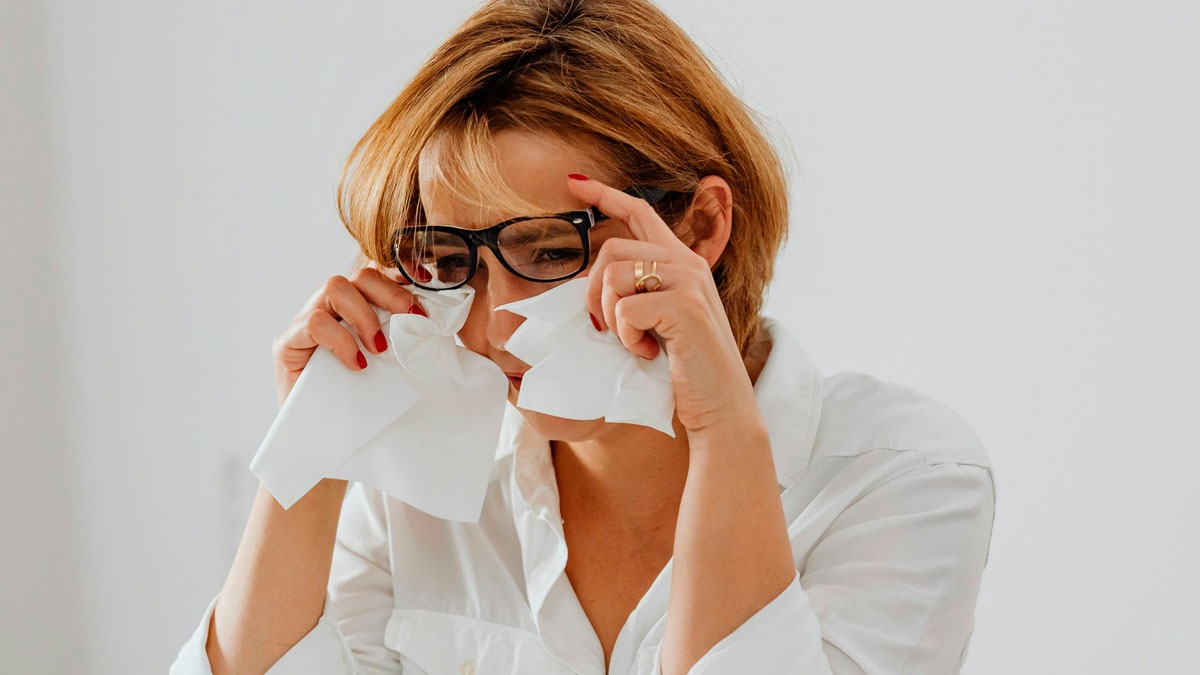 Woman with glasses wiping tears with tissues showing frustration linked to bosses being out of touch at work