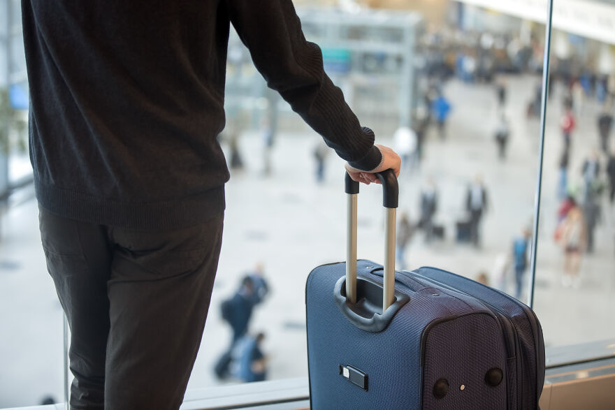 Person standing at airport window holding suitcase handle, capturing home alone vibes and travel abandonment scene. Person standing at airport window holding suitcase handle, capturing home alone vibes and travel abandonment scene.