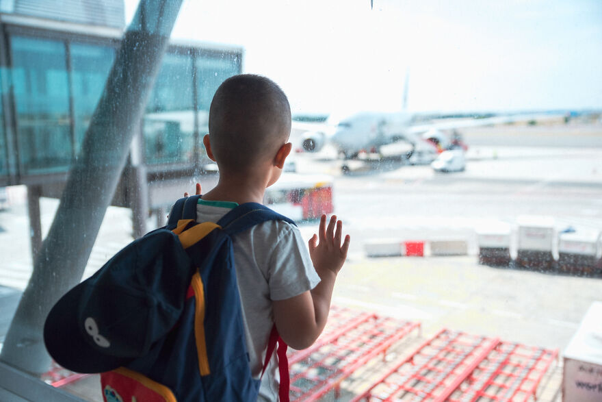 Young boy with backpack looking at airplane through airport window, capturing home alone vibes and child airport abandonment. Young boy with backpack looking at airplane through airport window, capturing home alone vibes and child airport abandonment.