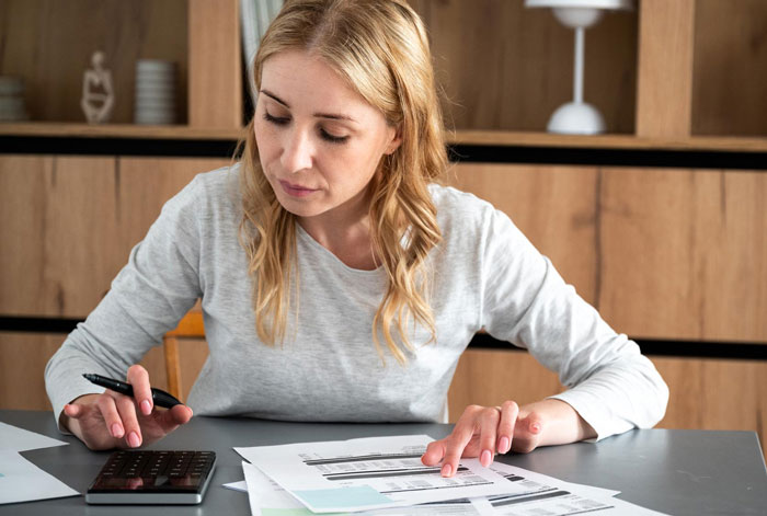 Woman using calculator and reviewing bills at home, illustrating parents forcing pay expensive rent challenges.