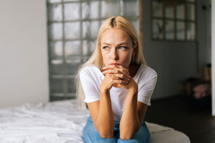 Young woman sitting on bed, looking worried and thoughtful about parents forcing pay expensive rent situation. Young woman sitting on bed, looking worried and thoughtful about parents forcing pay expensive rent situation.