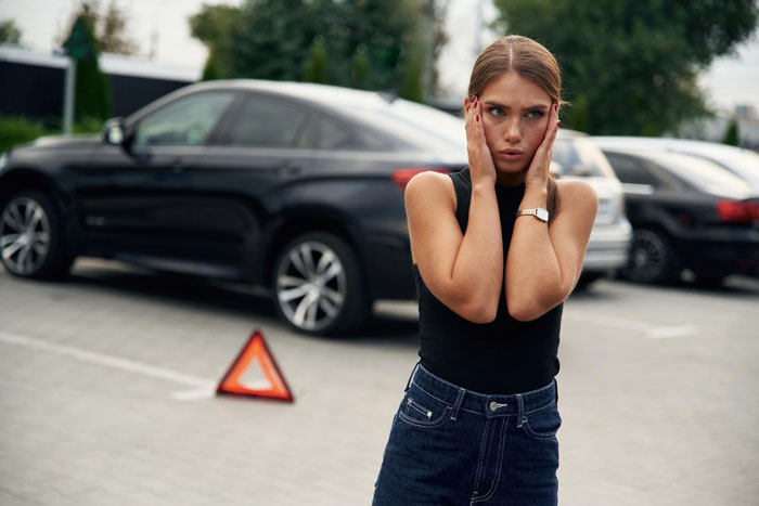 Woman looking frustrated in a parking lot next to a warning triangle, illustrating dodgy neighbor parking spot dispute. Woman looking frustrated in a parking lot next to a warning triangle, illustrating dodgy neighbor parking spot dispute.