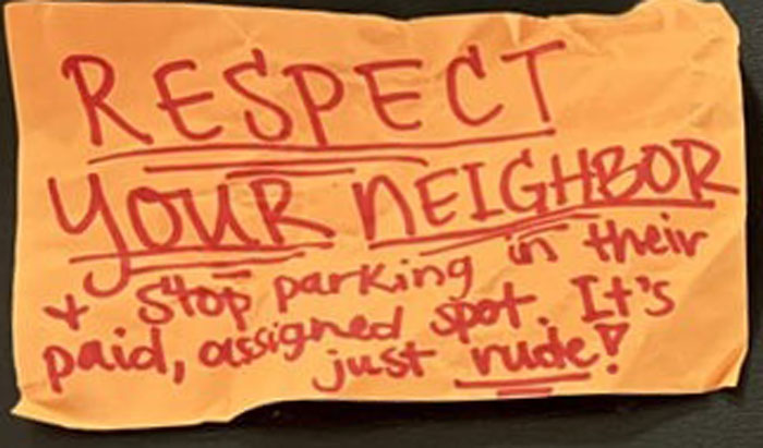 Handwritten anonymous note warning to respect neighbor's paid assigned parking spot and avoid rude parking behavior.