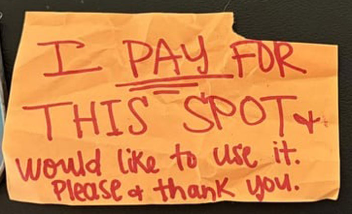 Handwritten anonymous note on orange paper attempting to claim a parking spot, related to dodgy neighbor parking dispute.