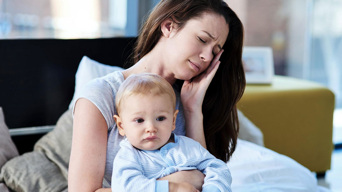 Tired mom with baby in her arms, showing exhaustion and stress from sleepless nights and fever care duties.