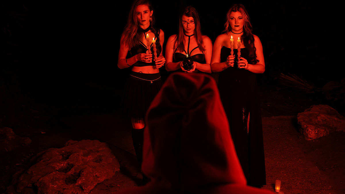 Three women holding candles and a skull in a dark setting, illustrating creative ways to avoid babysitting.