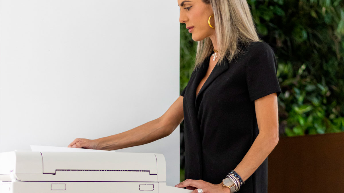 Woman in black shirt using a printer, illustrating stories of coworkers and office morons in a workplace setting.