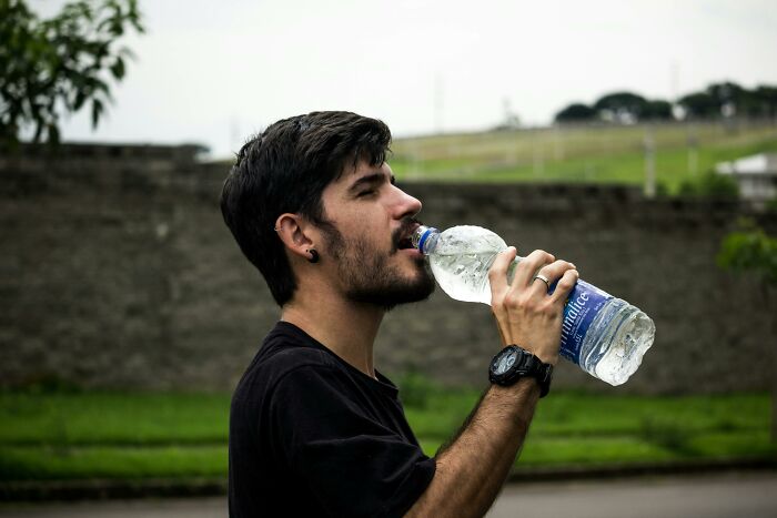 Young man drinking water from a plastic bottle outdoors, illustrating things people thought were a flex but aren’t.