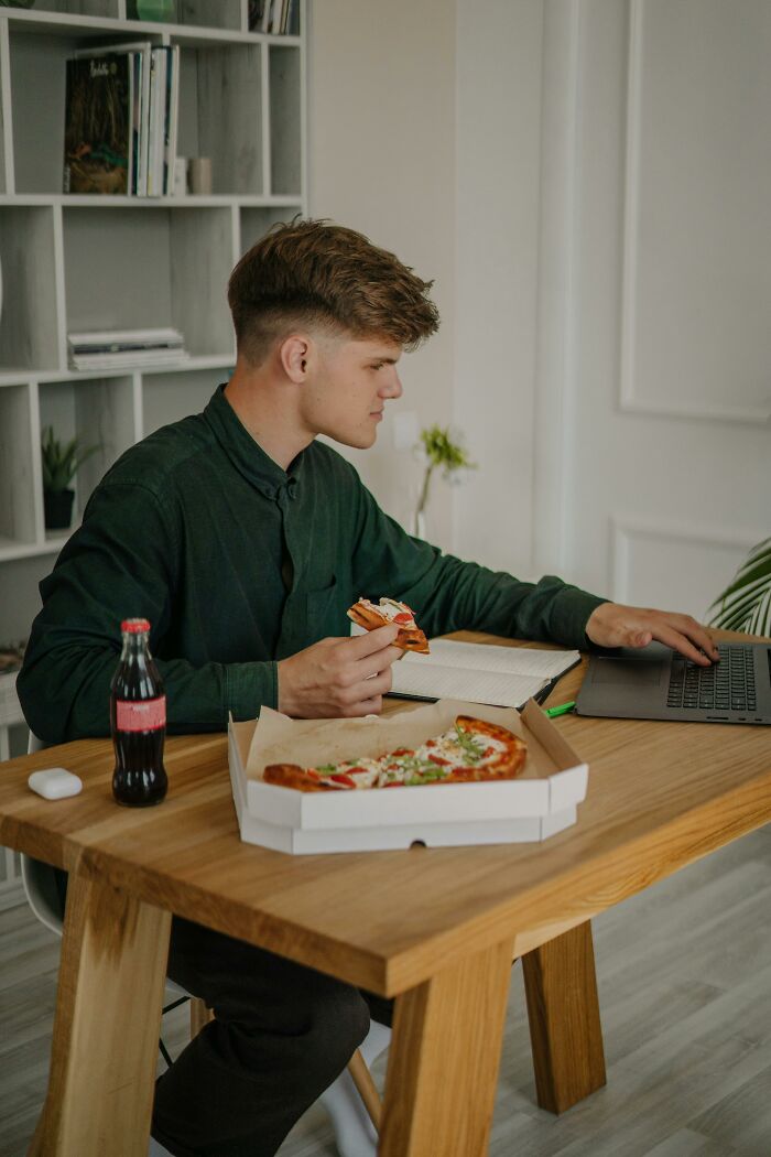 Young man eating pizza while working on laptop, illustrating common things people thought were a flex but actually aren’t.