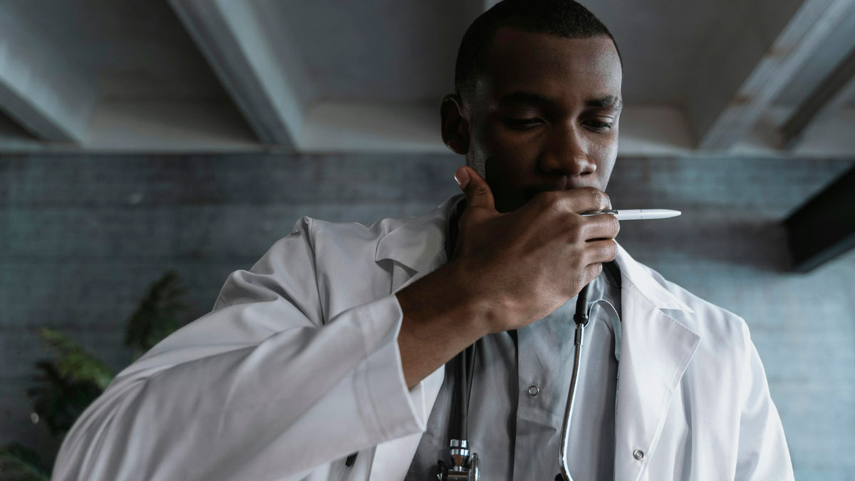 Doctor in a white coat looking thoughtful and disturbed while holding a pen, reflecting on disturbing facts.