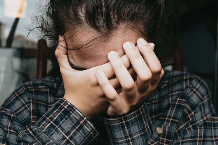 Woman covering face with hands, upset and emotional, expressing distress over family vacation and personal cramps. Woman covering face with hands, upset and emotional, expressing distress over family vacation and personal cramps.