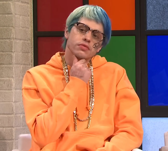 Pete Davidson in an orange hoodie and glasses, addressing scrutiny over size of his manhood in a TV show setting. Pete Davidson in an orange hoodie and glasses, addressing scrutiny over size of his manhood in a TV show setting.