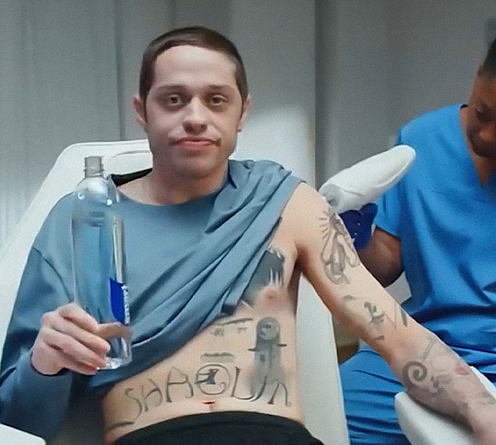 Pete Davidson sitting shirtless with tattoos, holding a water bottle during a medical or tattoo session. Pete Davidson sitting shirtless with tattoos, holding a water bottle during a medical or tattoo session.