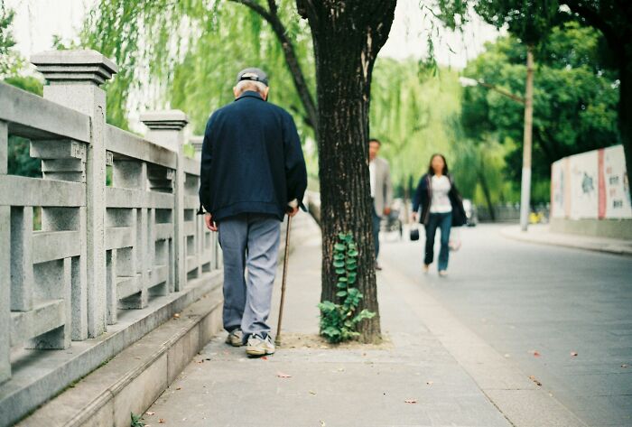 Elderly man walking with a cane on a tree-lined path illustrating challenges of shopping a*******n and non-substance dependencies.