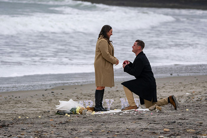 Man proposing on beach with bouquet, capturing a moment of heartbreak over wanting a rich husband not hardworking partner