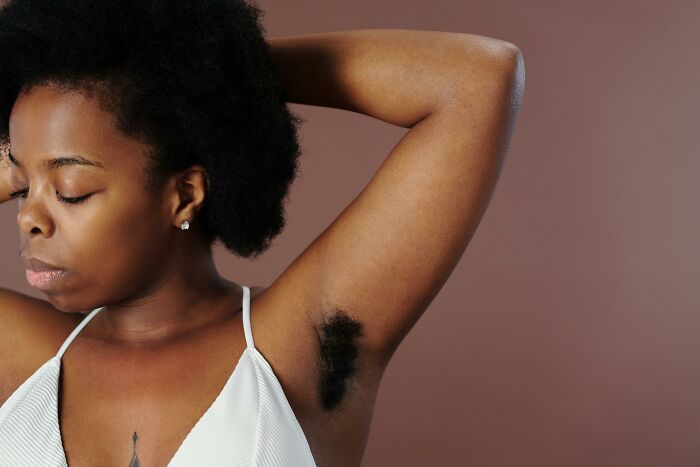 Black woman with natural hair wearing white top showing underarm hair, highlighting gender-based double standards concept.