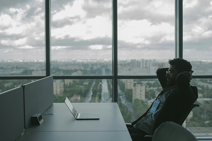 Man sitting back in office chair by laptop near window, reflecting on knowledge transfer before PTO and notice period. Man sitting back in office chair by laptop near window, reflecting on knowledge transfer before PTO and notice period.
