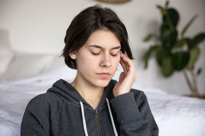 Young woman with closed eyes and hand on temple, appearing stressed while thinking about picking the wrong line at the grocery store.
