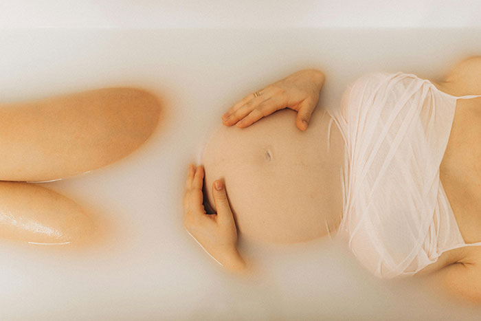 Heavily pregnant woman lying in a bathtub filled with milky water, hands resting on her belly. Heavily pregnant woman lying in a bathtub filled with milky water, hands resting on her belly.